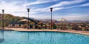 A pool area with lounge chairs and tables, surrounded by a fence, with a view of hills and trees in the background. - WOW! Smoky Mountains, 1 Bedroom Deluxe

 (Sevierville)