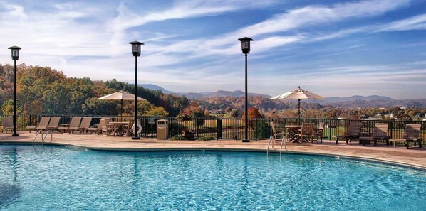 A pool area with lounge chairs and tables, surrounded by a fence, with a view of hills and trees in the background. - WOW! Smoky Mountains, 1 Bedroom Deluxe

 (Sevierville)
