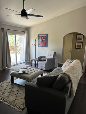 A living room with a ceiling fan, a grey armchair, a sofa, a coffee table, and a rug. - 4 Bedroom/3 Bath - Spacious Briargate Ranch Home with Office and WiFi near USAFA (Colorado Springs)