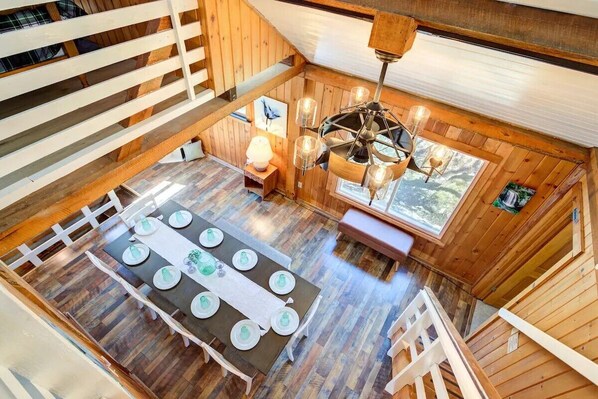 A wooden cabin with a dining area featuring a table set for six, a chandelier, and a window with a view of trees.