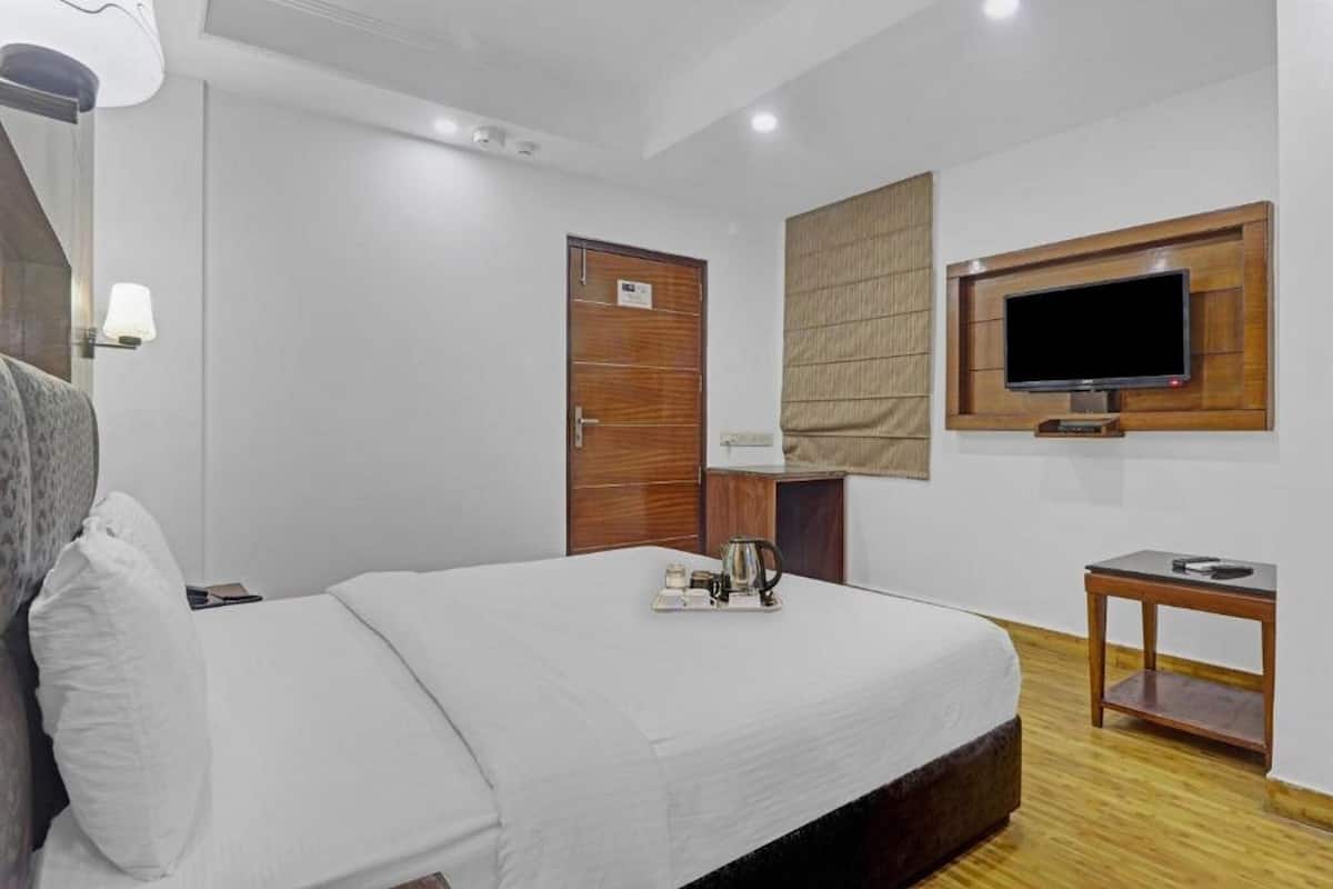 Ein Hotelzimmer mit einem Bett, einem an der Wand befestigten Fernseher, einer Holztür und einem kleinen Tisch mit einer Lampe.
