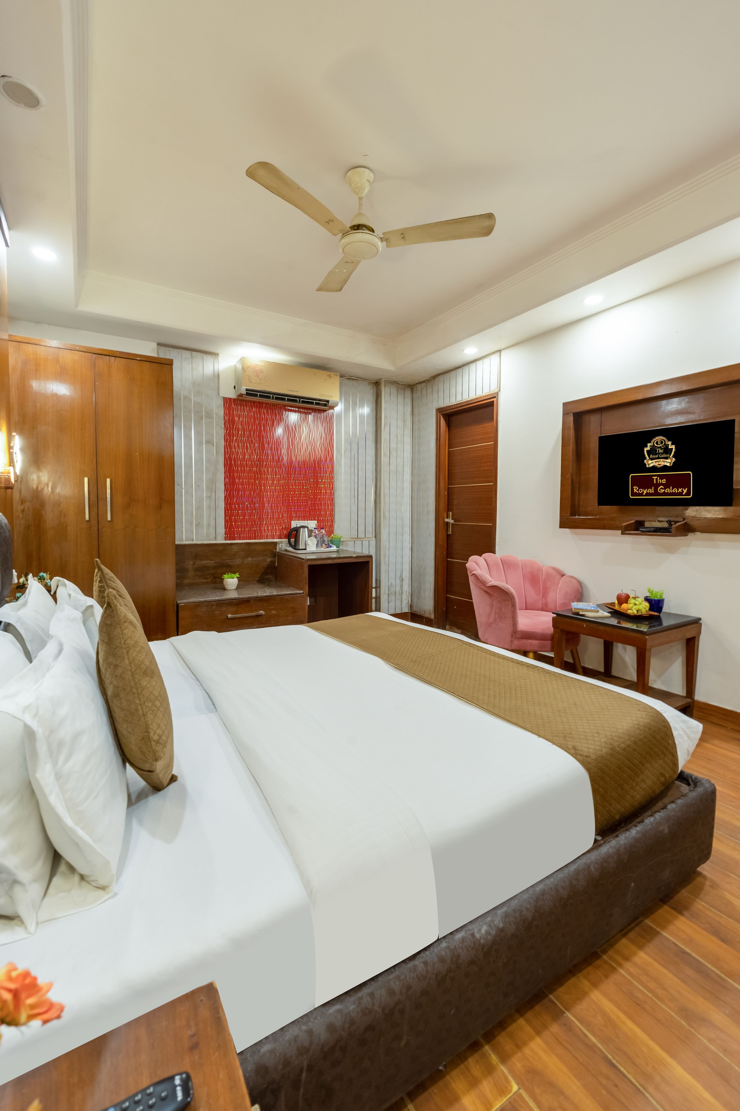 A hotel room with a bed, a desk, a chair, a television, and a ceiling fan.