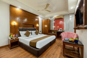 A hotel room with a large bed, wooden headboard, bedside tables, a desk, a chair, and a television.