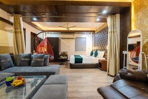 A modern hotel room with a sofa, a bed with a headboard, a glass coffee table with fruit, and a hanging chair. - The Royal Galaxy (New Delhi)
