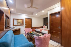 A hotel room with a bed, a sofa, a desk, a chair, and a ceiling fan. - The Royal Galaxy (New Delhi)