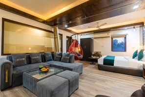 A modern living room with a sectional sofa, a glass coffee table, a hanging chair, a bed with a green blanket, and an air conditioning unit. - The Royal Galaxy (New Delhi)