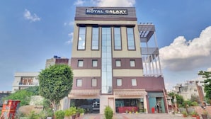 Ein Hotel namens "The Royal Galaxy Hotel" mit modernem architektonischen Design, das einen zentralen Eingang und zahlreiche Fenster an der Fassade zeigt.