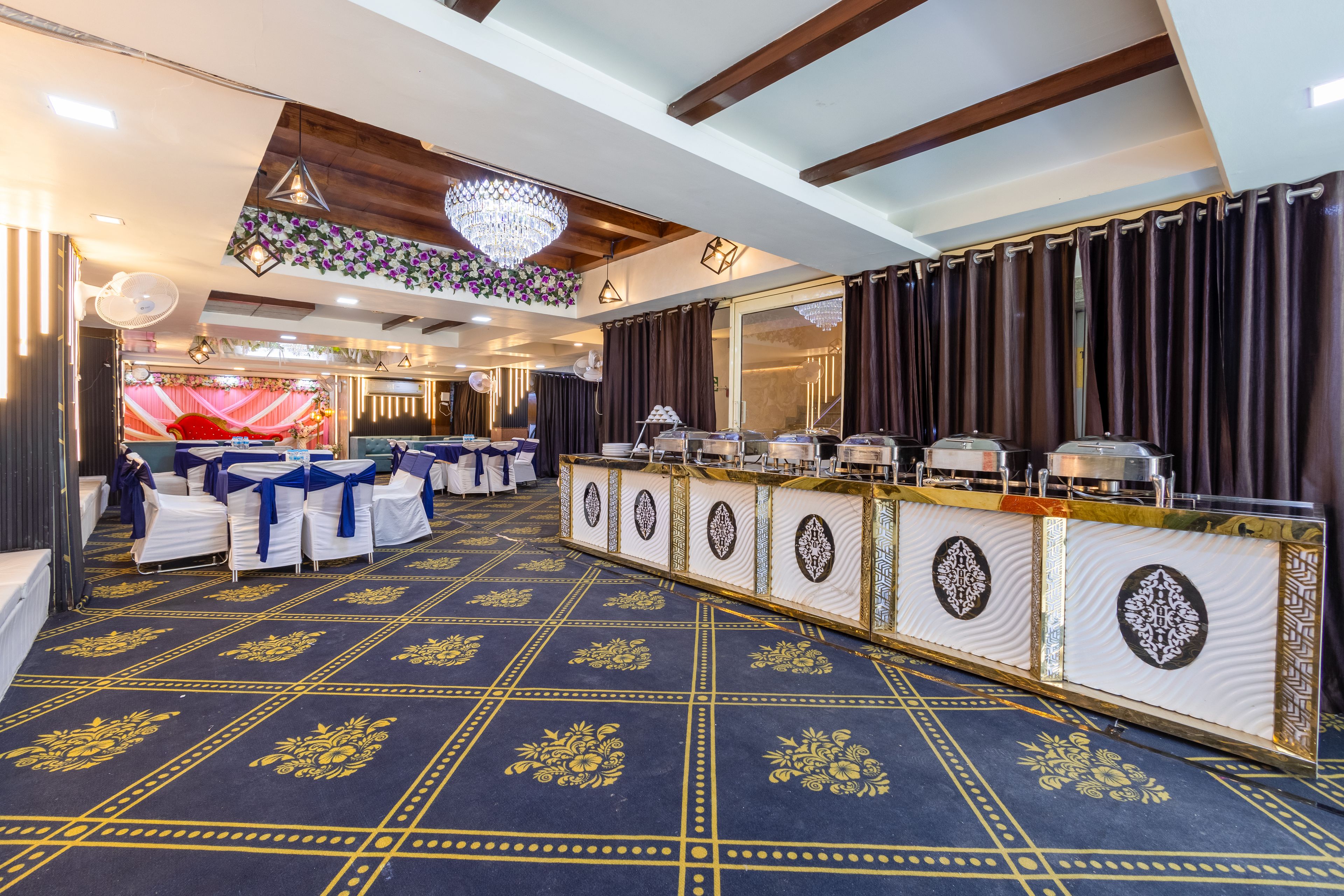 Un salón de banquetes con una larga barra, sillas con cintas azules y una alfombra estampada.