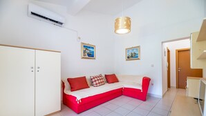 A room with a red and white sofa, a white wardrobe, and two framed pictures on the wall. - Modern accommodation just 450 metres from the sea (Baska)