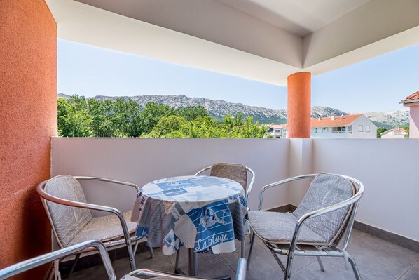 A balcony with a table and four chairs, overlooking a mountainous landscape with greenery and buildings in the background. - Modern accommodation just 450 metres from the sea (Baska)