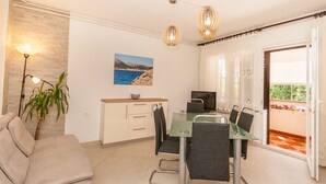 A dining area with a glass table, chairs, and a TV. There is a sofa and a plant in the corner. - Large flat with 3 air conditioning units, WiFi, BBQ, car park (Baska)