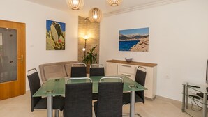 A dining area with a glass table, six chairs, a wooden bench, and a small kitchen area with a counter and a bowl. - Large flat with 3 air conditioning units, WiFi, BBQ, car park (Baska)