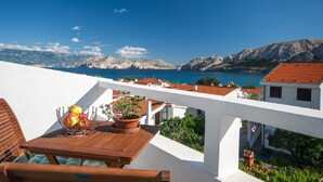 A terrace with a wooden table, potted plants, and a view of the sea and mountains. - Flat with sea view, air conditioning, WiFi, car park (Baska)