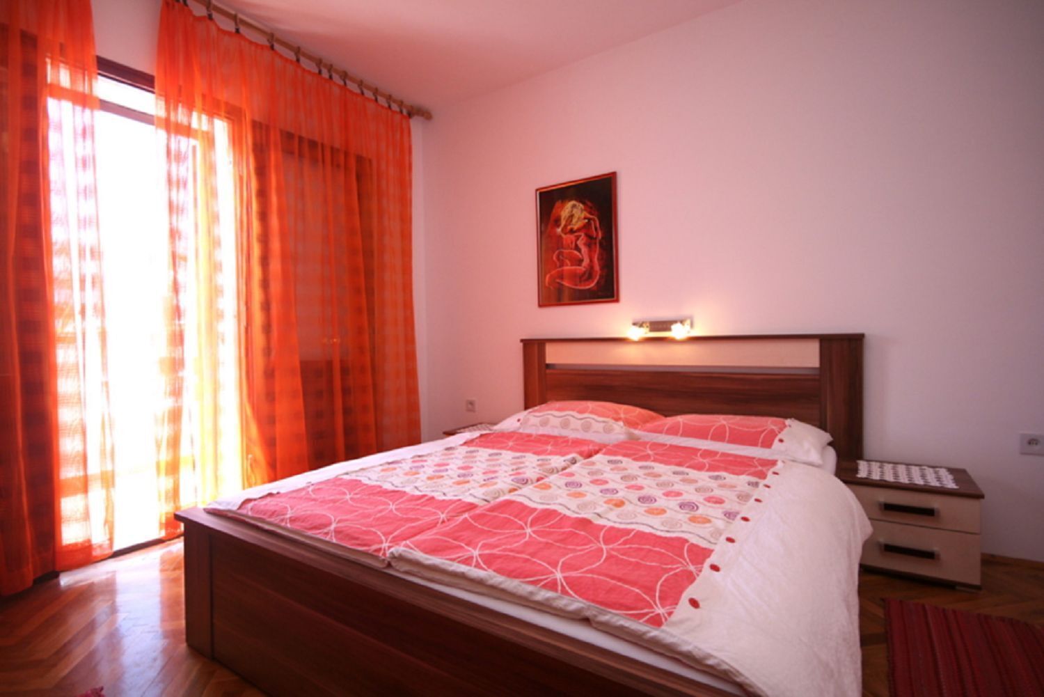 Una camera da letto con un letto in legno, un comodino, un tappeto rosso e un quadro appeso al muro.