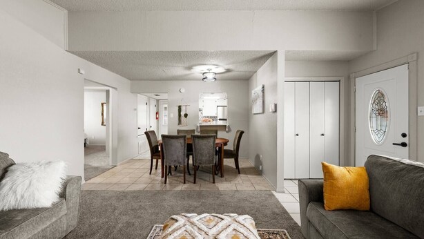 A spacious living room with a grey sofa, a patterned rug, and a dining area with a table and chairs.