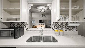 A kitchen with a built-in microwave, double sink, decorative backsplash, and a ceiling fan.
