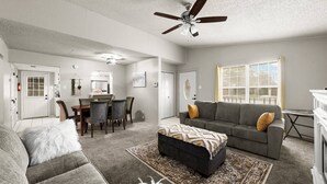 A spacious living room with a gray sofa, ottoman, and a dining area with chairs and a table.
