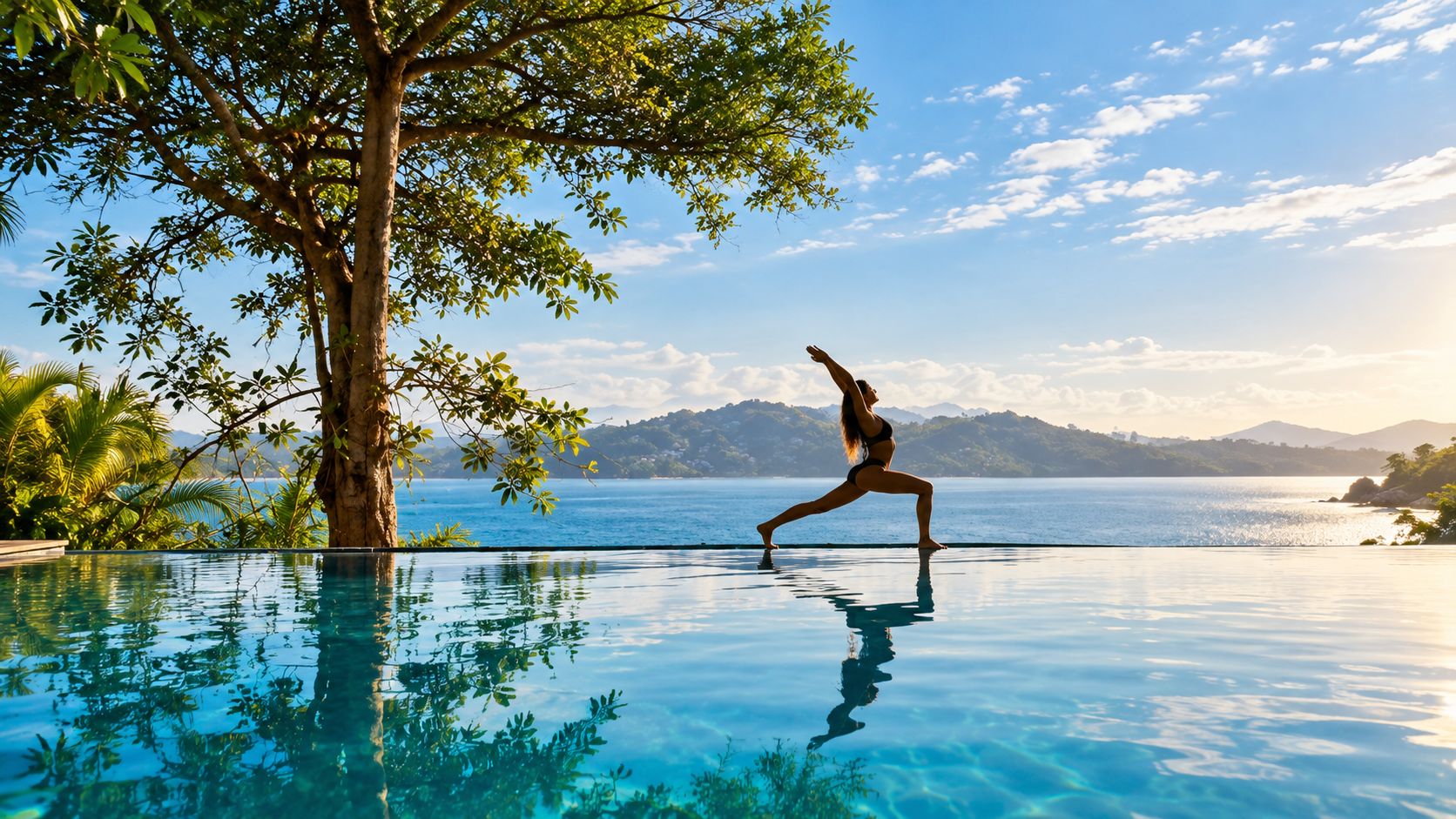 A person performing a yoga pose on a pool deck with a view of a body of water and mountains in the background.
