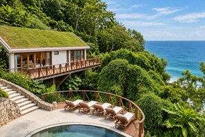 Una casa moderna con techo verde, piscina y terraza con sillones de descanso.
