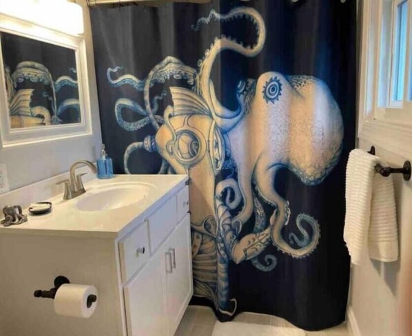 A bathroom with a sink, mirror, and a shower curtain featuring an octopus design.