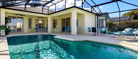 A swimming pool with clear water, surrounded by lounge chairs and a covered patio area.
