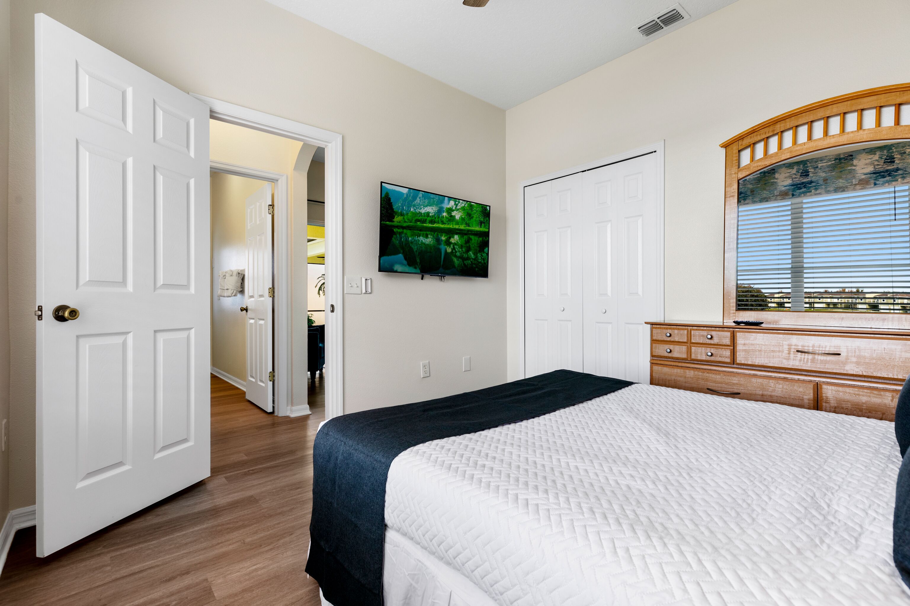 Quarto com cama, penteadeira, televisão e porta que dá para outro espaço.
