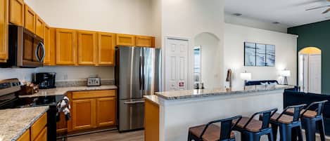 A modern kitchen with wooden cabinets, stainless steel appliances, and a bar area with stools.