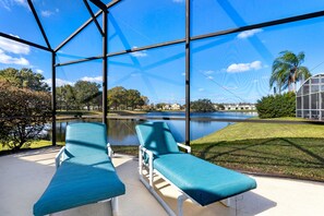 A covered outdoor area with two lounge chairs and a view of a lake and surrounding greenery. - Hills Bay Retreat (Davenport)