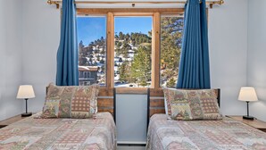 Une chambre avec deux lits, une fenêtre donnant sur un paysage de montagne enneigée et des arbres, et deux lampes de chevet.