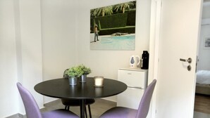 A small dining area with a round table, two purple chairs, a potted plant, a candle, and a painting of a pool scene on the wall. - Filoenia In Center of Athens (Athens)