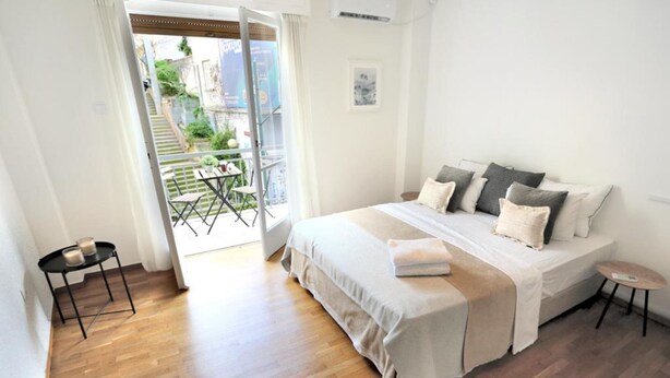 A bedroom with a large bed, a small table, and a view of a balcony with outdoor furniture. - Filoenia In Center of Athens (Athens)