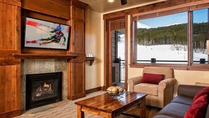 Una sala de estar acogedora con chimenea, televisor montado en la pared y un amplio ventanal con vistas a un paisaje nevado.