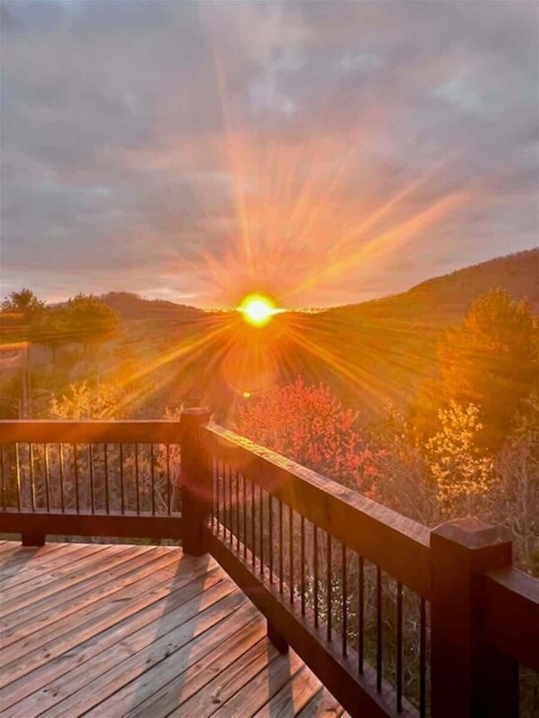 En træterrasse med gelænder med udsigt over et landskab i solnedgang.