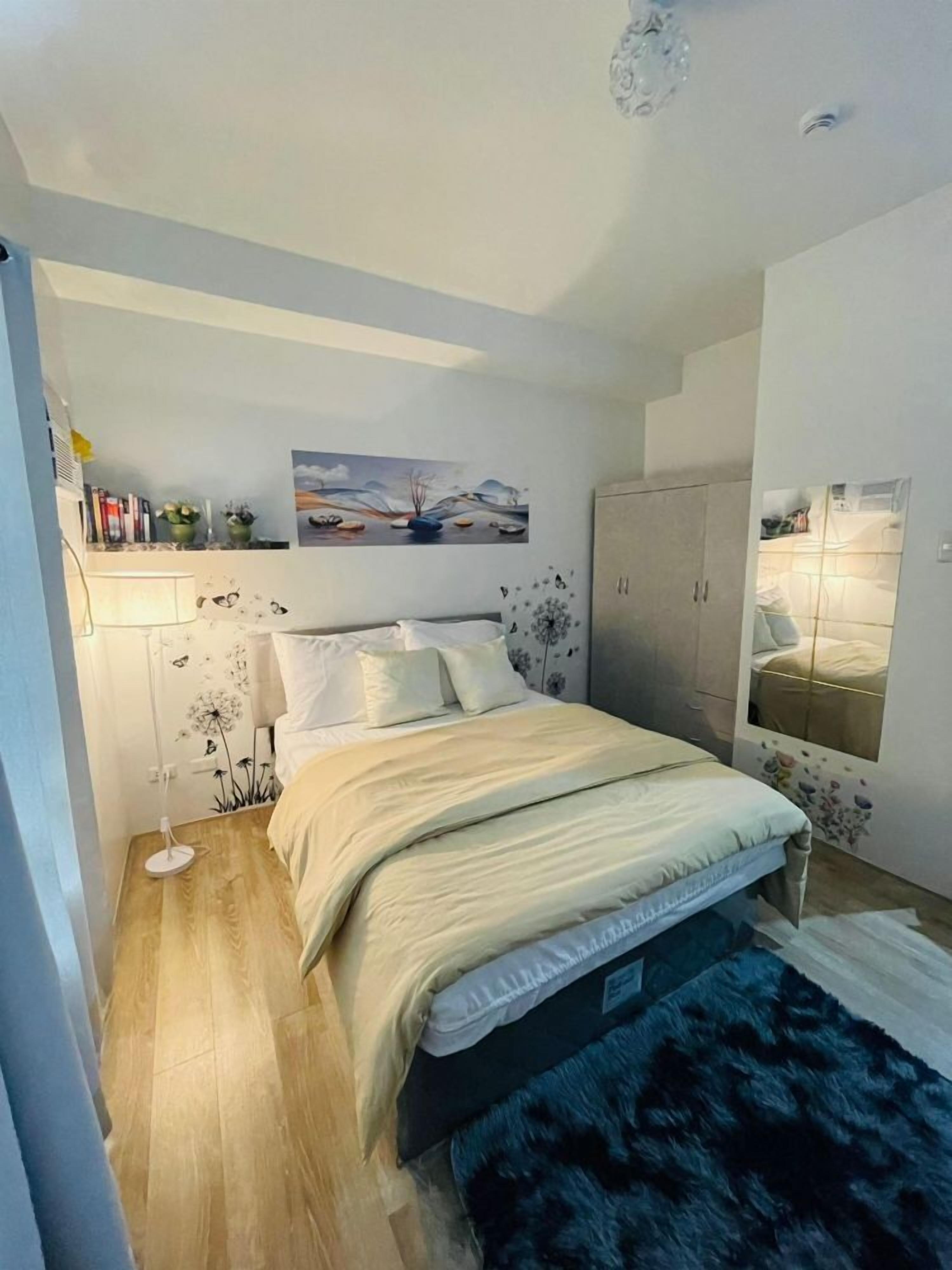 A bedroom with a bed, a nightstand, a dresser, and a wall-mounted mirror.