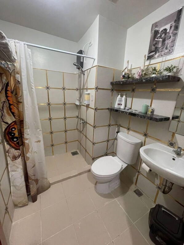 Un baño con ducha, inodoro, lavamanos y estantes con artículos de aseo.
