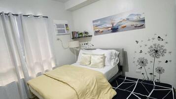 Een slaapkamer met een bed, een nachtkastje, een lamp, een raam met gordijnen, een wandairconditioner, een schilderij en een wanddecoratie van bloemen en vlinders.