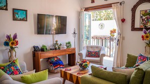 A living room with a TV, sofa, armchair, and a small table with a bowl of fruit. - Casa Eva 2 Bedroom Balcony Suite (Bucerias)