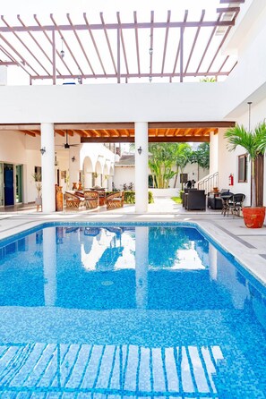 A swimming pool with a pergola overhead, outdoor seating area, and a view of a building in the background. - Casa Damián Standard Room (Bucerias)