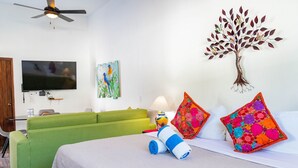 A hotel room with a green sofa, a bed with colorful pillows, a flat-screen TV, and a wall art piece. - Casa Huapango Studio suite with kitchenette. (Bucerias)