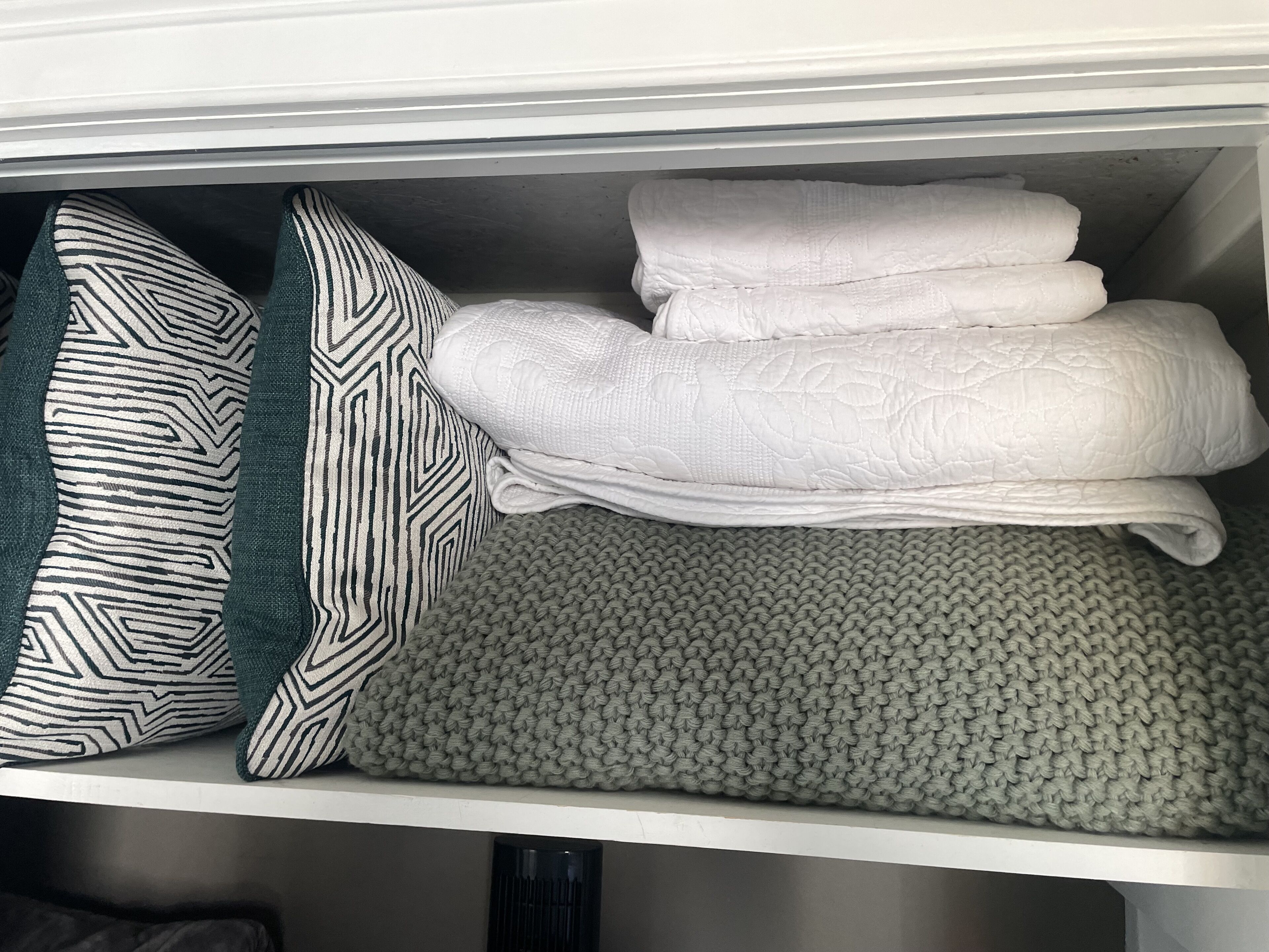 A neatly organized storage area with folded towels and a patterned pillow.