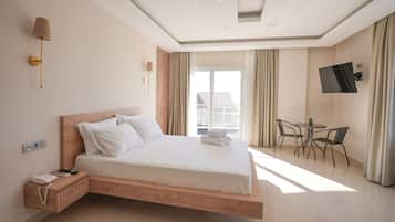 Una habitación de hotel moderna con una cama grande, mesita de noche, lámpara, televisor y un balcón con mesa y sillas.