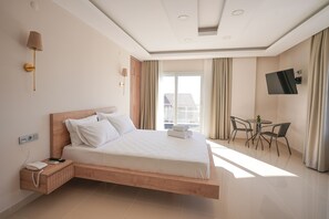 A modern hotel room with a large bed, bedside table, lamp, TV, and a balcony with a table and chairs. - Soul House Kuşadası (Kusadasi)