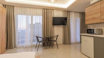 Ein modernes Hotelzimmer mit einem Bett, einem Esstisch mit Stühlen, einem an der Wand befestigten Fernseher, einer Mikrowelle und einem kleinen Kühlschrank.