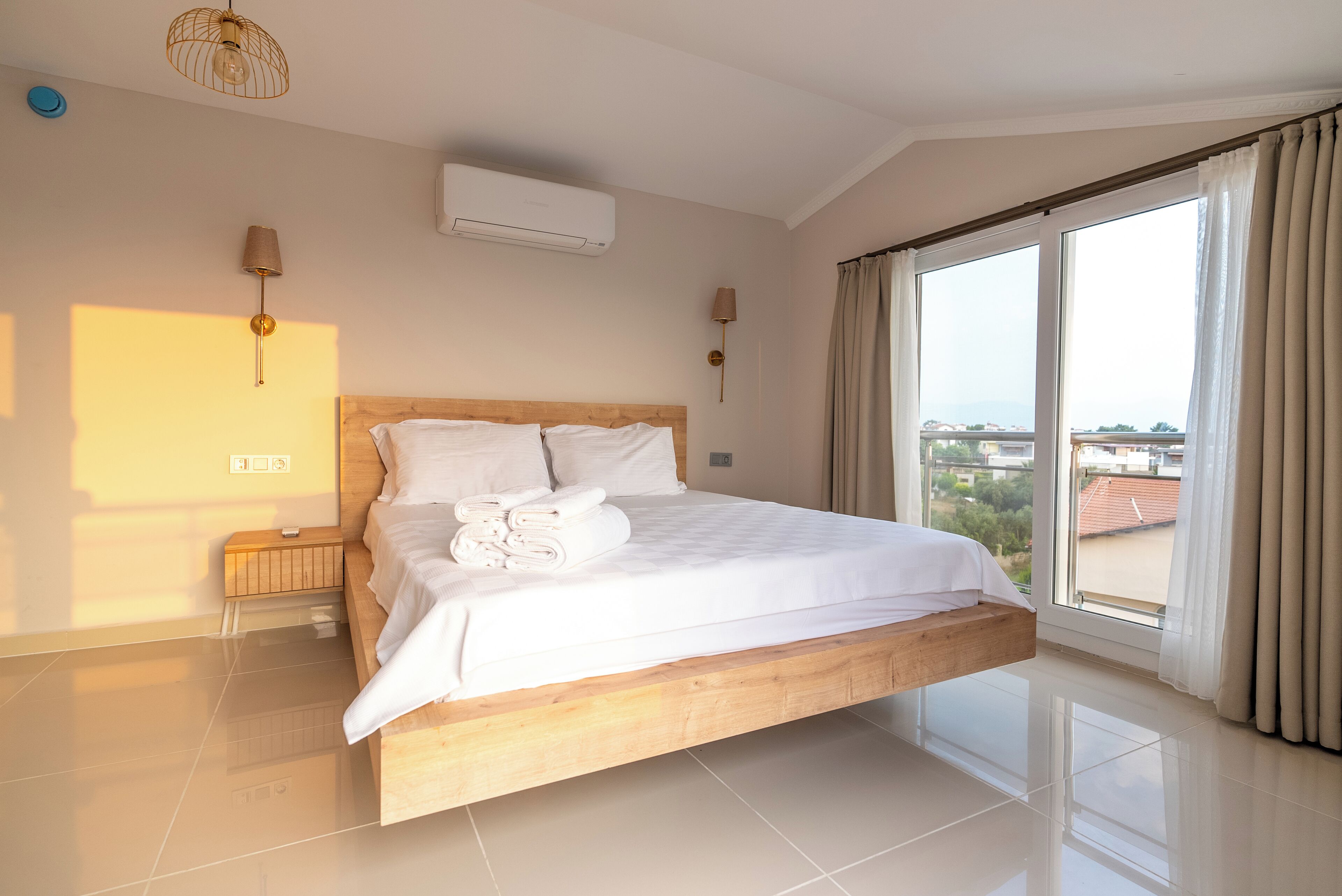 Un dormitorio moderno con una cama de madera, ropa de cama blanca y un amplio ventanal con cortinas.