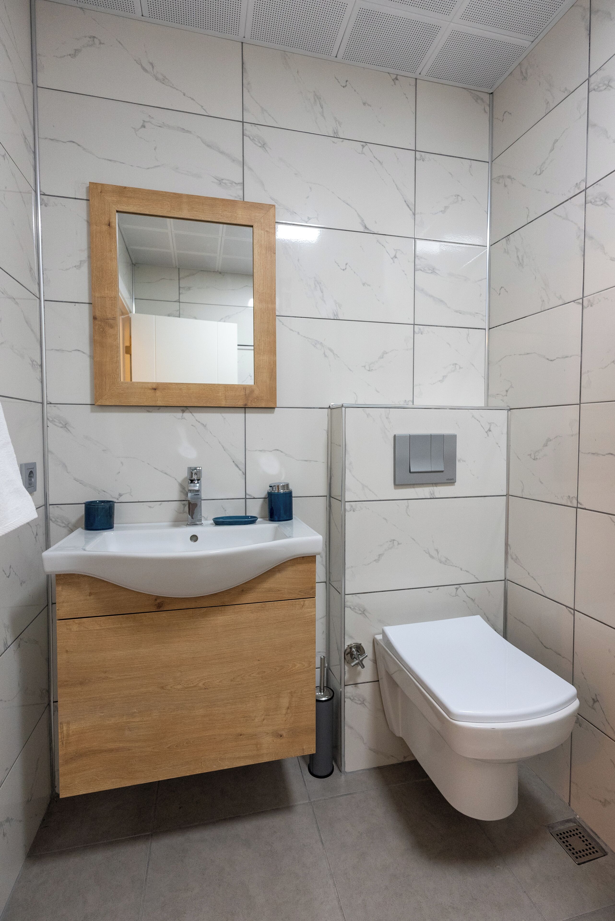 A bathroom with a wooden vanity, a white sink, a mirror, and a toilet.