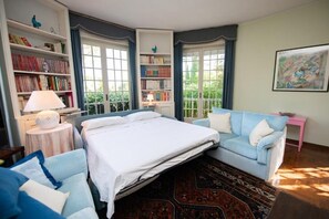 Un dormitorio con una cama, un sofá azul, una estantería y una ventana con cortinas.