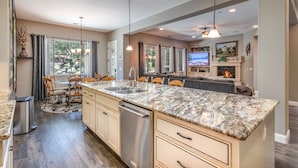 A modern kitchen with granite countertops, stainless steel appliances, and a dining area with wooden chairs.