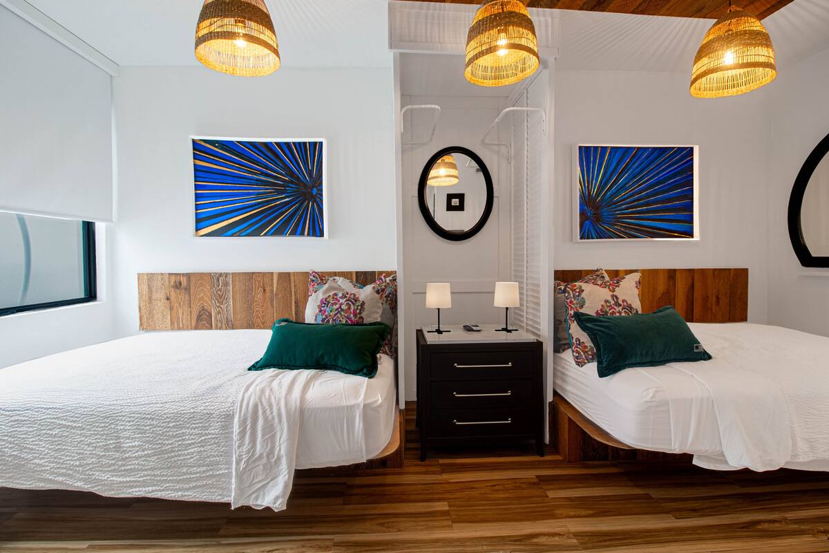 A double room with two beds, wooden headboards, a small bedside table with lamps, and artwork on the walls.