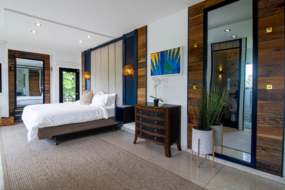 A modern bedroom with a large bed, a dresser, and a mirror.