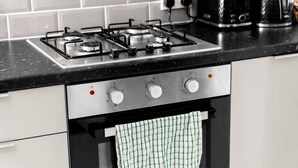 Una cocina con estufa a gas, horno y un toalla verde y blanca a cuadros colgada.